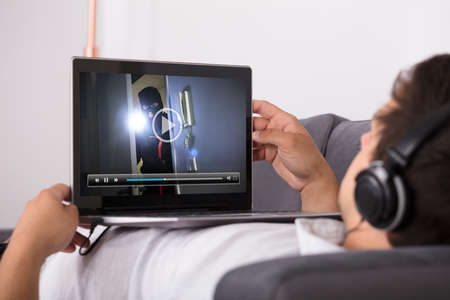 Close-up of a man watching thriller movie on laptopの写真素材