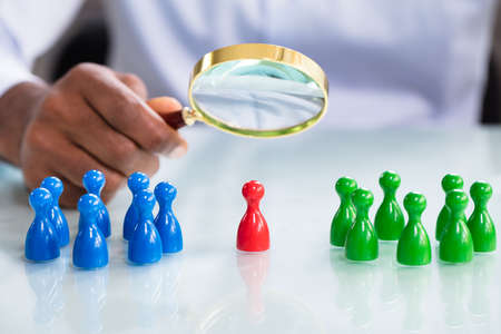 A Male Looking At Colorful Pawns With Magnifying Glass On The Reflective Deskの写真素材