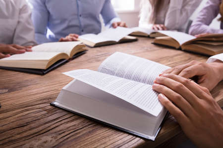 Group Of People Reading Bible On Wooden Desk