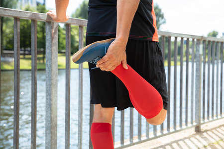 Close-up Of A Male Runner Stretching His Leg In Front Of Riverの写真素材