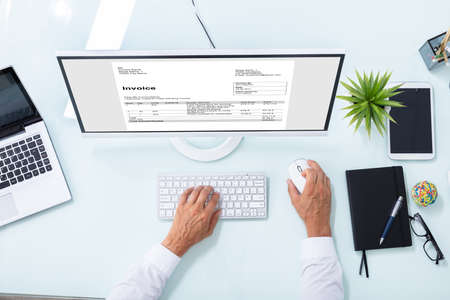 Elevated View Of A Businessman's Hand Checking Invoice On Computerの写真素材