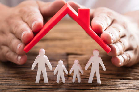 A person's hand protecting family figures with red roof on wooden deskの写真素材