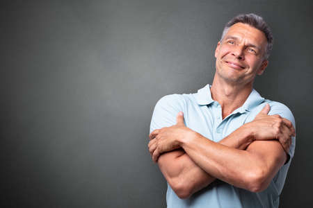 Portrait Of A Mature Man Hugging Himself Against Grey Backgroundの写真素材