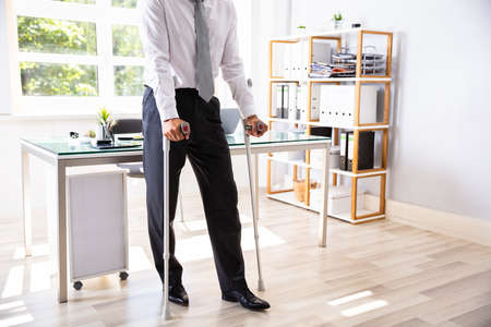 Disabled Businessman With Crutches Standing In Officeの写真素材