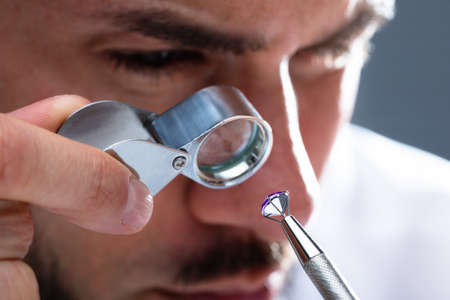 Close-up Of A Male Jeweler's Hand Looking At Diamond Through Magnifying Loupeの写真素材