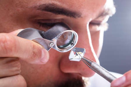 Close-up Of A Male Jeweler's Hand Looking At Diamond Through Magnifying Loupeの写真素材
