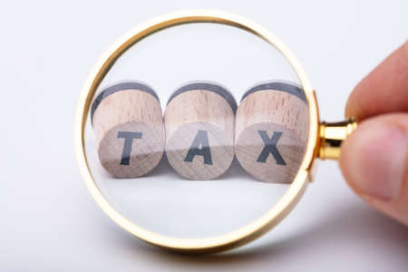 A Person Looking At Tax Word On Cork Through Magnifying Glassの写真素材