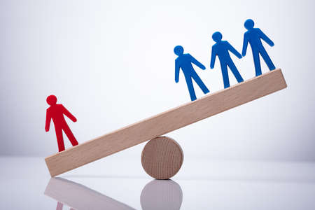 Red Human Figure Standing Against Blue Team On Wooden Seesawの写真素材