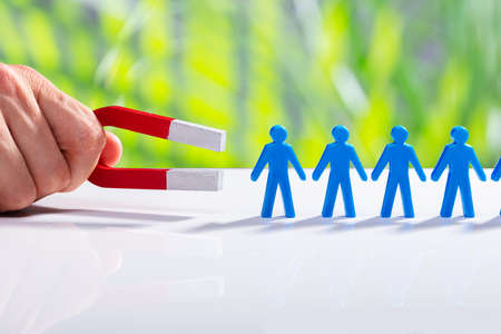 Businessman's Hand Attracting Blue Human Figures Standing In A Row With Horseshoe Magnetの写真素材