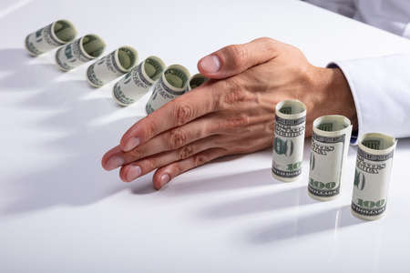 High Angle View Of A Person Stopping Falling Rolled Up Banknotes On Deskの写真素材