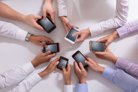 Group Of Businesspeople Using Smartphone Over White Desk
