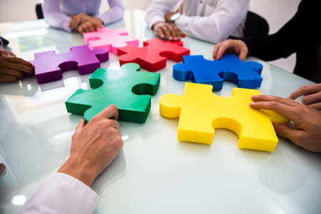 Group Of Businesspeople Colorful Solving Jigsaw Puzzle On Desk In Office
