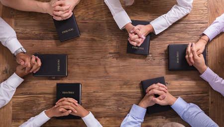 High Angle View Of People's Praying Hands On Holy Bibleの写真素材