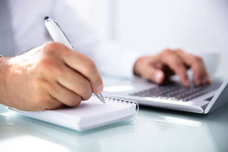 Close-up Of A Businessman's Hand Writing In Diary Over Desk