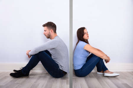 Side View Of A Unhappy Young Couple Sitting Back To Back At Home