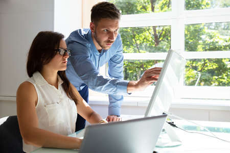 Businessman Standing Near Businesswoman Pointing At Computer Screen