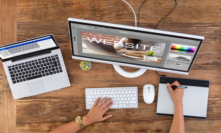 Female Designer's Hand Using Graphic Tablet While Creating Website On Computer