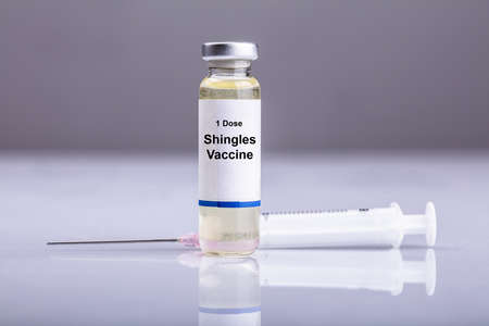 Close-up Of Shingles Vaccine And Syringe On Reflective Deskの写真素材