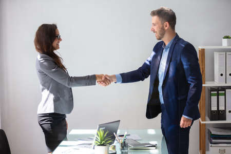 Smiling Young Businesswoman Shaking Hands With Her Partner In Officeの写真素材