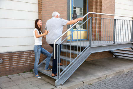 Rear View Of A Young Daughter Assisting Her Senior Father Climbing Staircase