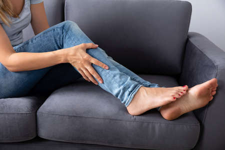 Woman Sitting On Sofa Looking At Her Injured Leg