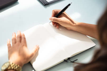 Close-up Of A Businesswoman Writing In Notebook With Pen Over Desk