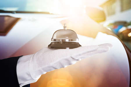 Close-up Of A Person's Hand Holding Service Bell In Front Of Carの写真素材