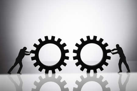 Silhouette Of Two Businesspeople Joining Gears On Reflective Backgroundの写真素材