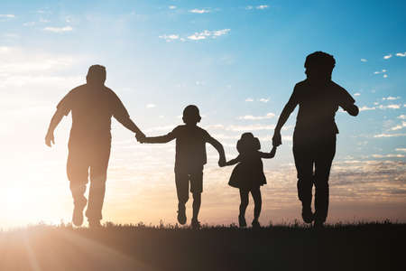 Silhouette Of Family Running In Park Against Sky At Sunsetの写真素材