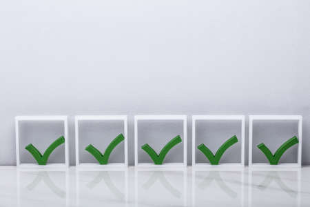 Row Of Green Check Marks In Boxes On Reflective Deskの写真素材