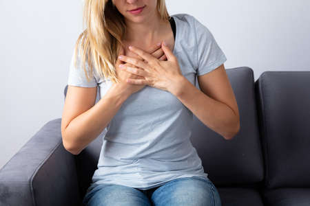 Woman Sitting On Sofa Having Chest Painの写真素材