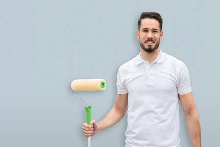 Portrait Of A Smiling Young Painter With Paint Roller On Gray Backgroundの写真素材