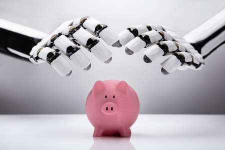 Robotic Hand Protecting Pink Piggybank Over Reflective Deskの写真素材