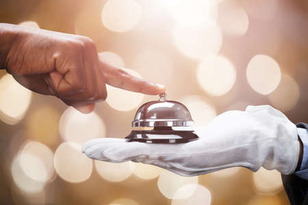 Customer's Hand Ringing Service Bell Held By Butler On Bokeh Backgroundの写真素材