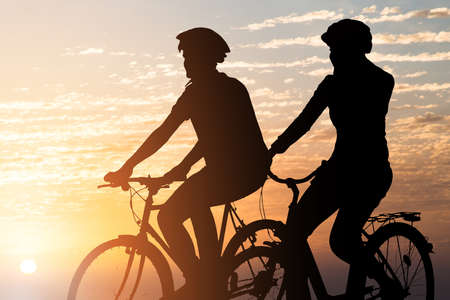 Silhouette Of A Couple Riding Bicycle At Sunsetの写真素材