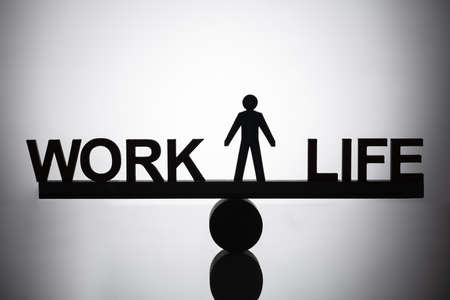 Silhouette Of A Human Figure Standing Between Work And Life Balance On Seesawの写真素材