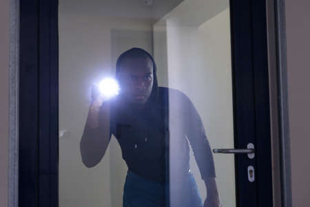 Thief Looking Through Glass Door With Flashlightの写真素材