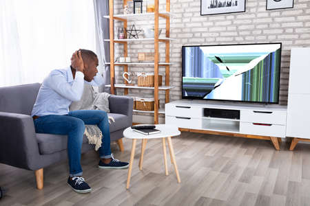 African Man Sitting On Couch Looking At Broken TVの写真素材