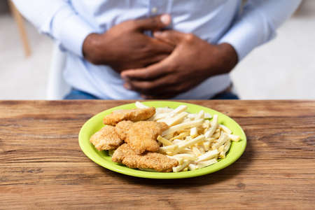Fried Food On Plate In Front Of Man Having Stomach Painの写真素材