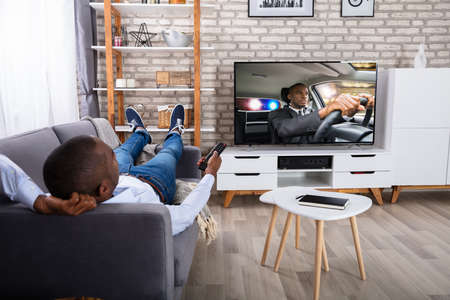 Man Lying On Sofa Watching Television At Home