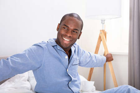Portrait Of A Happy Young African Man Sitting On Bedの写真素材