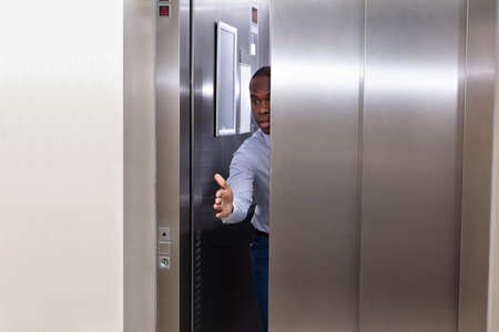 Young African Man Trying To Stop Elevator Door With His Handの写真素材