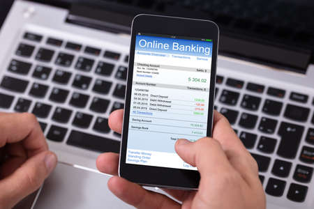 Close-up Of A Person Doing Online Banking On Mobile Phone Over Laptop