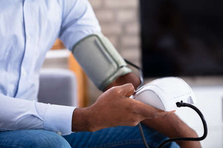 Young Man Sitting On Sofa Checking His Blood Pressure At Home