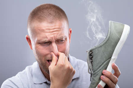 Close-up Of A Man Covering His Nose While Holding Stinky Shoe On Grey Backgroundの写真素材
