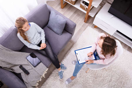 Girl Sitting On Sofa Explaining Her Problems To Female Psychiatrist At Homeの写真素材