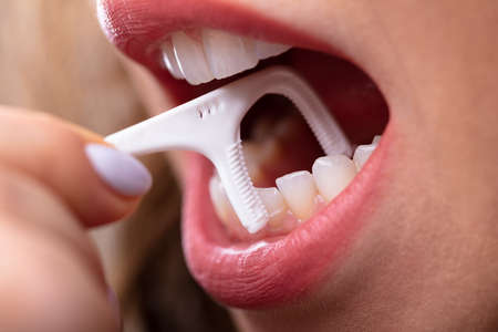 Close-up Of A Woman's Hand Cleaning Teeth With Dental Flossの写真素材