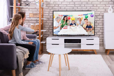 Mother And Daughter Sitting Together On Sofa Watching Television In Living Room