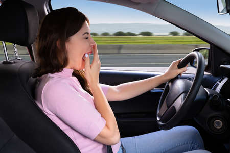 Side View Of A Beautiful Young Woman Yawning While Driving Car