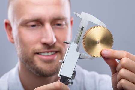 Close-up Of A Man Measuring Gear's Size With Digital Electronic Vernier Caliper On Grey Background